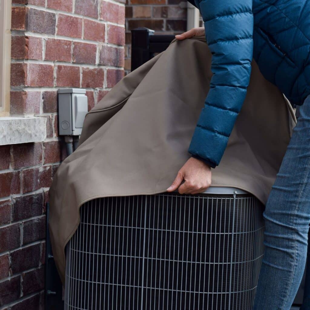 man maintaining his ac unit in fall and winter by covering it up