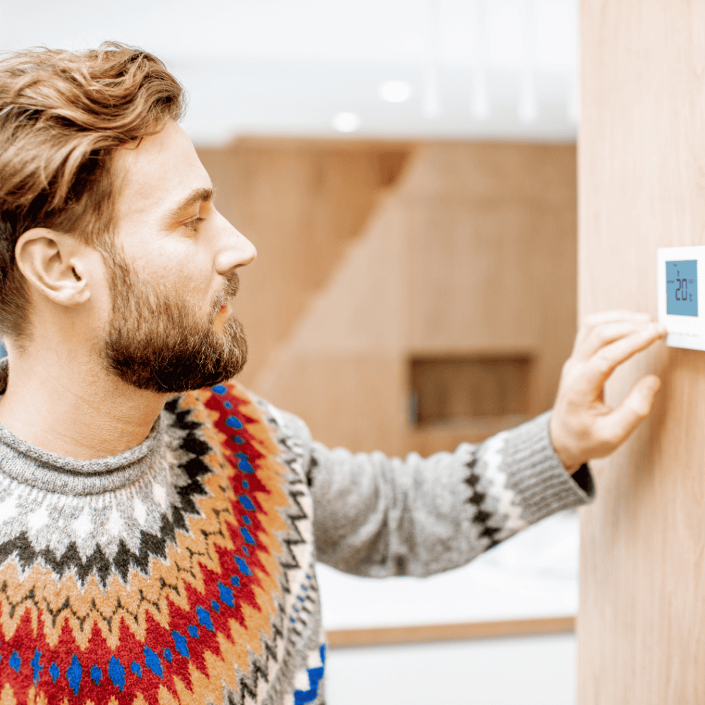 man lowering thermostat to lower heating costs during winter